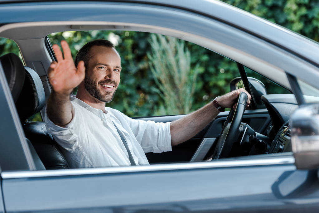 67361cd59e38f97e87ef9377_stock-photo-selective-focus-happy-man-driving-car-waving-hand